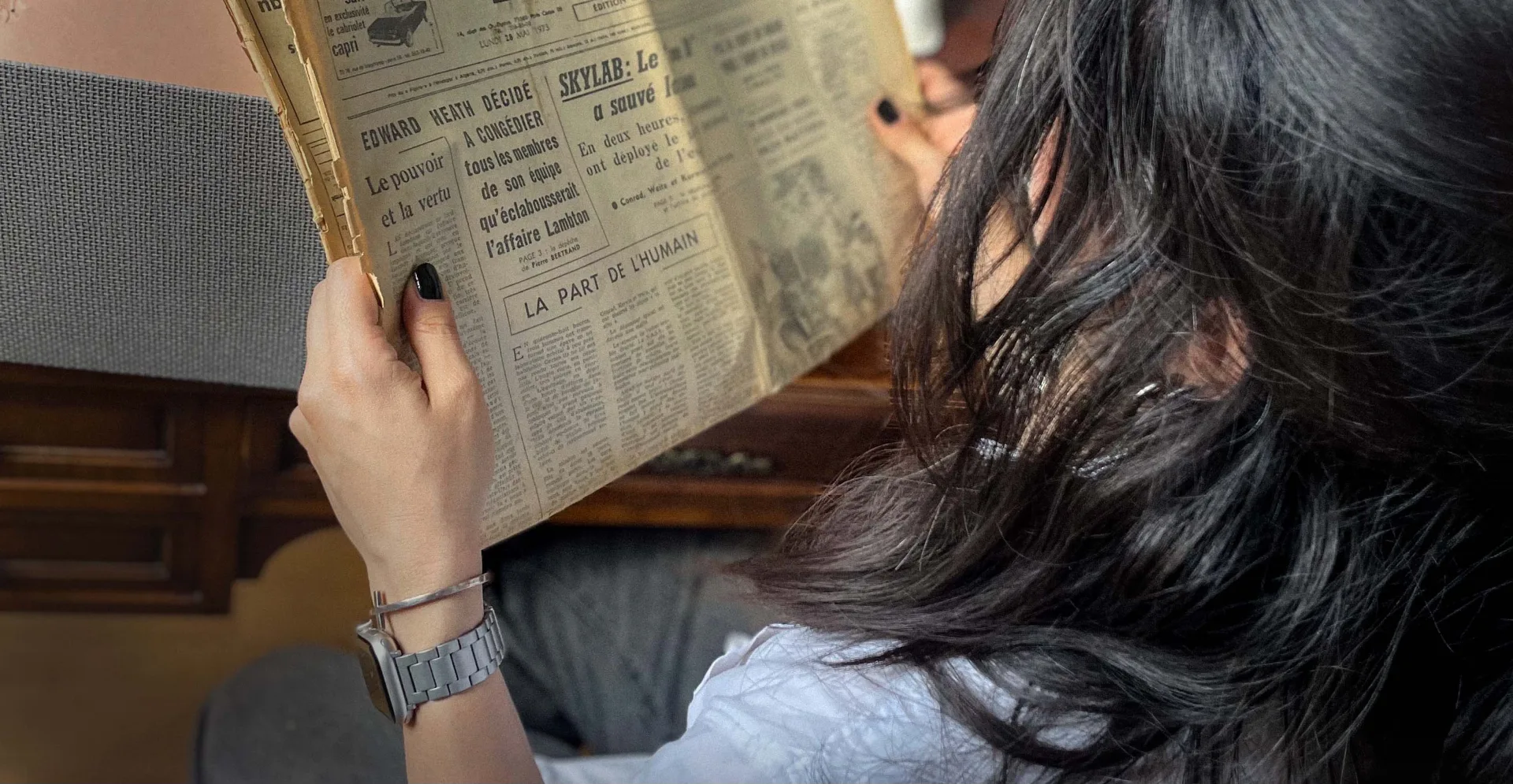 A woman reading an aged fictional newspaper in warm light.