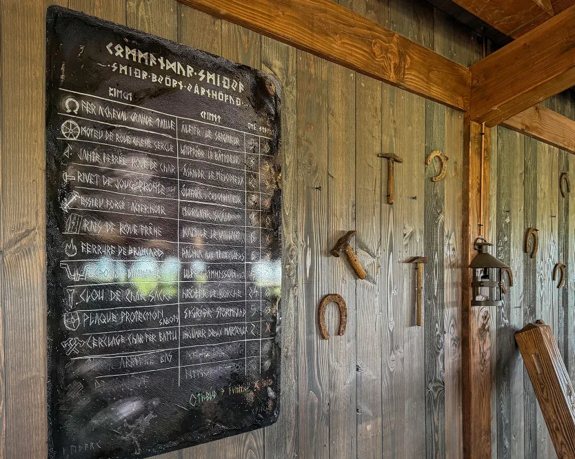 Runic chalkboard menu on a wood-clad wall, with a horseshoe and forge tools.